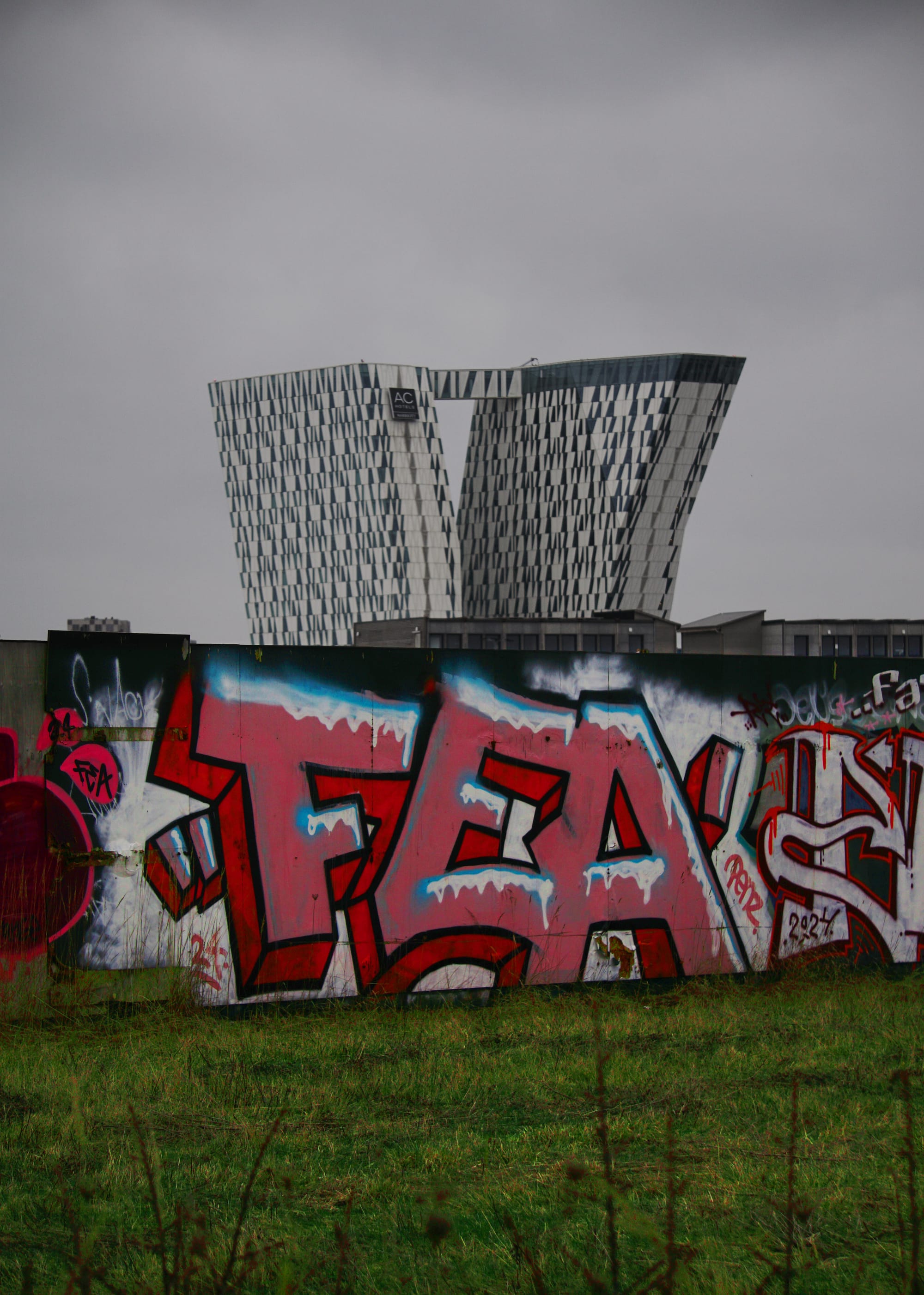A temporary wall with colourful grafiti dominates the lower half of the image, with a modern building emerging above it in the upper half