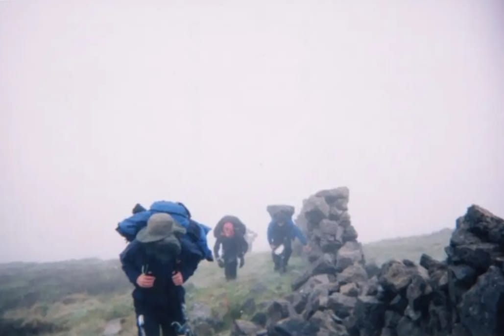 Some fellas climbing a mountain on a very foggy day beside the Mourne Wall